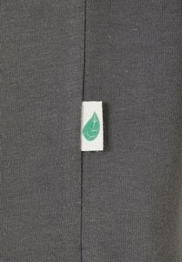 Icône de feuille verte sur une petite étiquette en tissu blanc cousue dans la couture d'un tissu tricoté gris foncé.