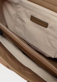 Εσωτερικό μπεζ τσάντας με θήκη με φερμουάρ, που διαθέτει απαλή υφή υφάσματος και λογότυπο από καφέ δέρμα.