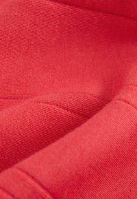 Tessuto rosso con una finitura morbida e testurizzata; presenta cuciture e pieghe sottili, evidenziando un materiale leggero e traspirante.