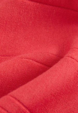 Rode textiel met een zachte, gestructureerde afwerking; beschikt over subtiele stiksels en plooien, wat een lichtgewicht, ademende stof laat zien.