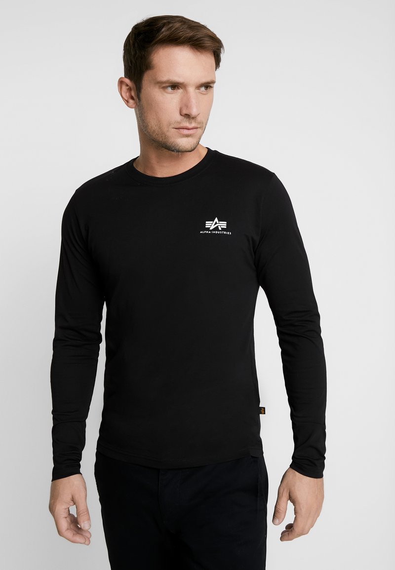 Schwarzes Langarm-T-Shirt aus glattem Stoff, mit einem kleinen weißen Logo auf der Brust. Einfacher runder Halsauschnitt und taillierte Passform.