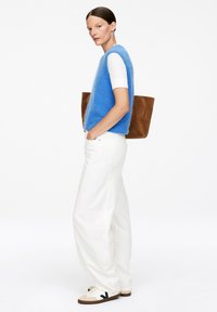 Blauer, flauschiger Strickpullover über einem weißen T-Shirt mit kurzen Ärmeln, kombiniert mit weißen, weiten Hosen und einer beigefarbenen Wildledertasche. Braune und weiße Sneaker.