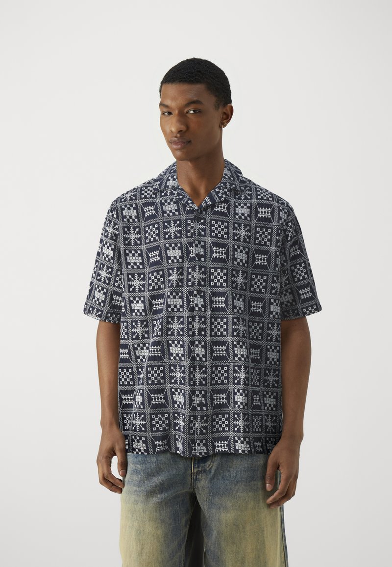 Korte mouwen shirt in marineblauw met witte geometrische patronen, met een klassieke kraag en een ontspannen pasvorm. Gepaarde met vervaagde lichte spijkerbroek.