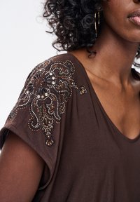 Brązowa krótka bluzka z krótkim rękawem i głębokim dekoltem w serek, ozdobiona misternymi koralikami i cekinami na ramieniu w czarnych, srebrnych i brązowych odcieniach.