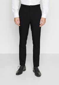 Pantaloni eleganti neri con vestibilità slim, caratterizzati da una texture liscia, davanti piatto e chiusura con un solo bottone. Indossati con scarpe eleganti nere.