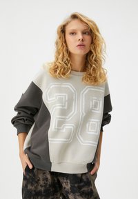 Sudadera en gris claro y gris oscuro con un gran gráfico en blanco del "28". Fabricada en tejido suave, presenta mangas largas y puños acanalados.