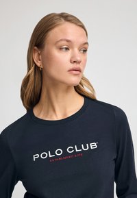 Camicia a maniche lunghe navy con "POLO CLUB" e "FONDATO NEL 2012" ricamati in bianco e rosso. Presenta un collo rotondo e una texture morbida.