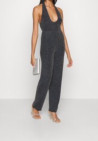 Svart, glittrande halterneck jumpsuit med djup V-ringning, vida ben och figurnära midja. Silverfärgad kuvertväska och nakna klackar med remmar fulländar looken.