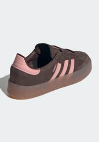 Low-top brown suede sneaker with pink leather heel tab and three pink side stripes, translucent gum sole, and "SAMBA" label.