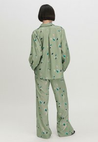 Groene, gemusterde tweedelige outfit met een losvallend shirt en brede broekspijpen met abstracte vormen in roze, blauw en zwart.