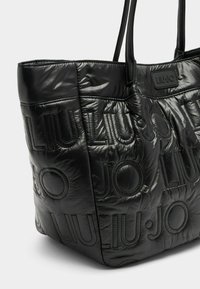 Fekete steppelt bevásárlótáska fényes anyagból, dombornyomott logó részletekkel és két masszív fogantyúval. Simogató textúrájú, strukturált formájú.