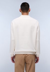 Felpa girocollo in off-white, con orlo e polsini ribattuti, texture liscia e vestibilità rilassata. Abbinata a pantaloni color khaki.