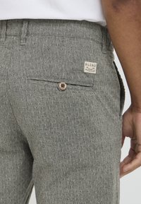 Gray patterned trousers made of textured fabric with a back pocket, button closure, and a branded label displayed on the waistband.