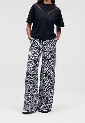 Žena v černém krátkém tričku s krajkovými detaily a vysokým pasem široké kalhoty se vzorem černobílých zebřích pruhů.