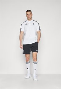 Hvit polo skjorte med korte ermer, svarte detaljer og Juventus-logo, kombinert med svarte shorts, hvite sokker med svarte striper og hvite sko.