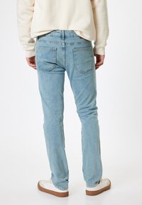 Ljust blå denimjeans med rakt ben, två bakfickor och synliga söm detaljer, tillsammans med vita sneakers.
