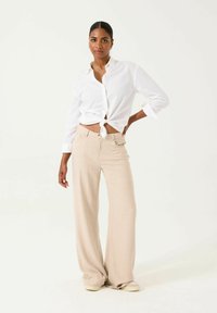 Camisa blanca de botones con un nudo en la cintura, combinada con pantalones de pierna ancha beige. Tejido suave y corte relajado; diseño minimalista.