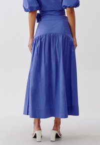 Abito blu fluente con maniche a sbuffo, vita cin cinata e gonna a pieghe. Presenta un tessuto testurizzato e un dettaglio con cravatta sul retro.