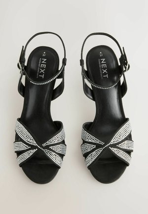 Svarta mocka sandaletter med klack och korsande design prydda med silverfärgade strassstenar och en smal ankelrem. Platt sula för komfort.