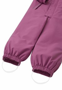 Paarse waterdichte overall met elastische manchetten en voetstraps. Zachte, gladde textuur. Voorzien van drukknoopsluitingen en een ritszak.