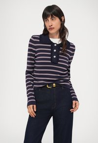 Top de manga larga a rayas azul marino y rosa con cuello con volantes y tapeta de botones, combinado con pantalones vaqueros oscuros y un cinturón negro.