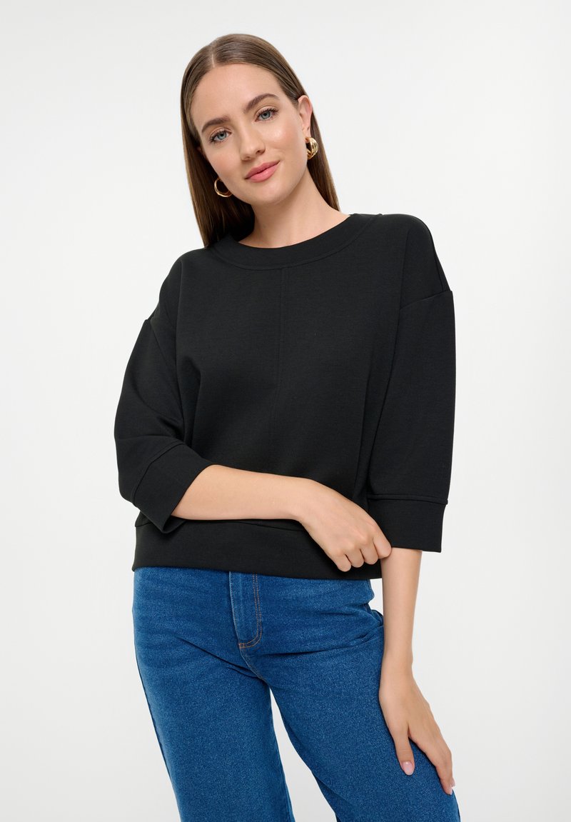 Zwarte oversized sweatshirt met een ronde hals en driekwartmouwen, gecombineerd met blauwe denim jeans. Gladde stoftextuur.