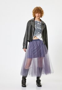 Sort læder bikerjakke, grafisk cropped top, lagdelt lilla tylskirt, knæhøje sorte støvler med spænder, afslappet og moderne design.