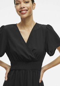 Must mustriga mustriga kleit lühikeste puffvarrukatega, smockitud talje ja pehme voolava kangaga. V-kaelus. Sile tekstuur minimaalsete detailidega.