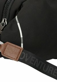 Bolsa de nailon negra con un acento de cuero marrón texturizado. Cuenta con un cierre de cremallera y una correa impresa con la palabra "ADVENTURE" en letras grandes.