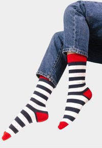 Skarpetki w paski w kolorze granatowym i białym z czerwonymi akcentami przy mankiecie, pięcie i palcach. Materiał wydaje się miękki o gładkiej strukturze.