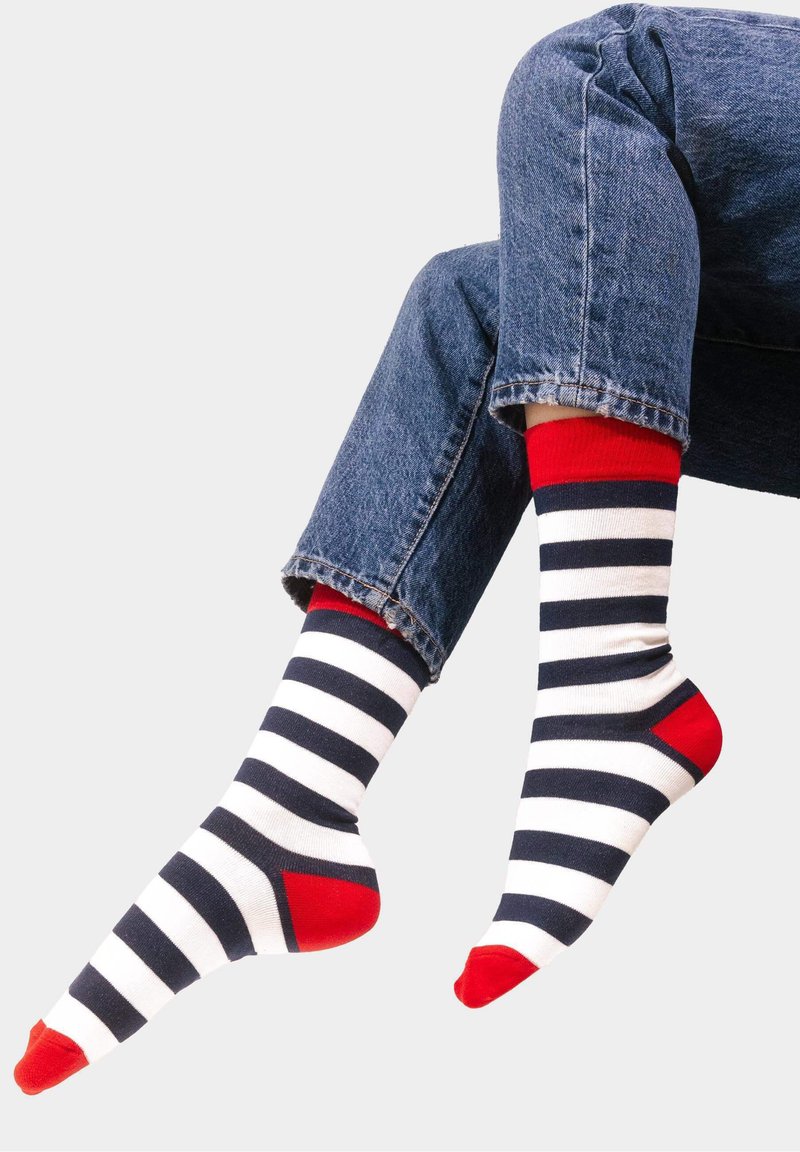 Skarpetki w paski w kolorze granatowym i białym z czerwonymi akcentami przy mankiecie, pięcie i palcach. Materiał wydaje się miękki o gładkiej strukturze.