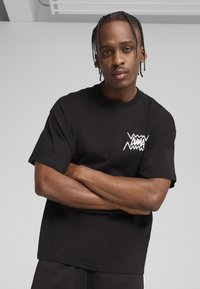 Sort bomulds t-shirt med et hvidt grafisk logo på venstre bryst. Korte ærmer, afslappet pasform og en glat overflade.