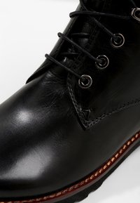 Chaussure habillée en cuir noir poli avec des lacets noirs passant par quatre œillets métalliques et bord de semelle marron cousu.