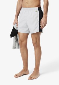 Mannen zwemshorts in lichtgrijs en zwart. Elastische tailleband, zijzakken en een klein groen logo detail aan de linkerkant. Zacht, sneldrogend stof.