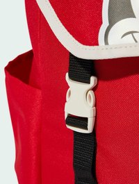 Zaino rosso con bordi bianchi e chiusura con fibbia in plastica. La tracolla è nera con superficie testurizzata, che migliora la presa e la durabilità.