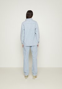 Zestaw z jasnoniebieskiej dżinsowej kurtki i spodni, charakteryzujący się luźnym krojem, mankietami na guziki oraz minimalistycznymi przeszyciami na neutralnym tle.