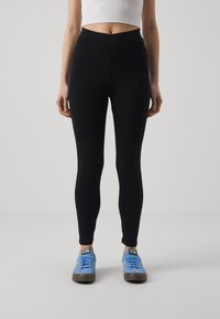 Black leggings made of stretchy fabric, featuring a high waist and a slim fit, paired with blue sneakers. Simple, seamless design.