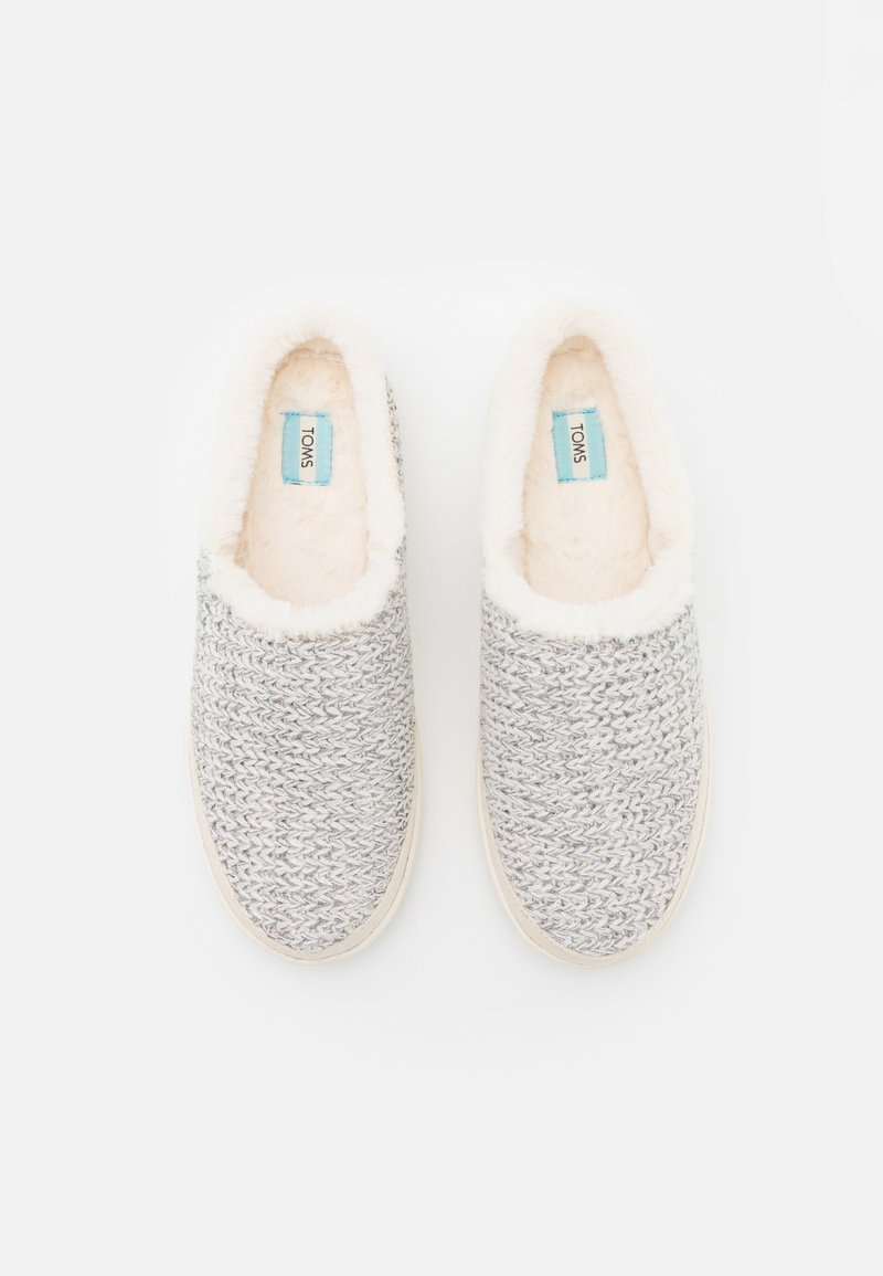 Pantofole grigie tessute senza lacci con rivestimento morbido bianco, caratterizzate da una punta arrotondata e una suola di colore chiaro. Logo TOMS visibile all'interno.