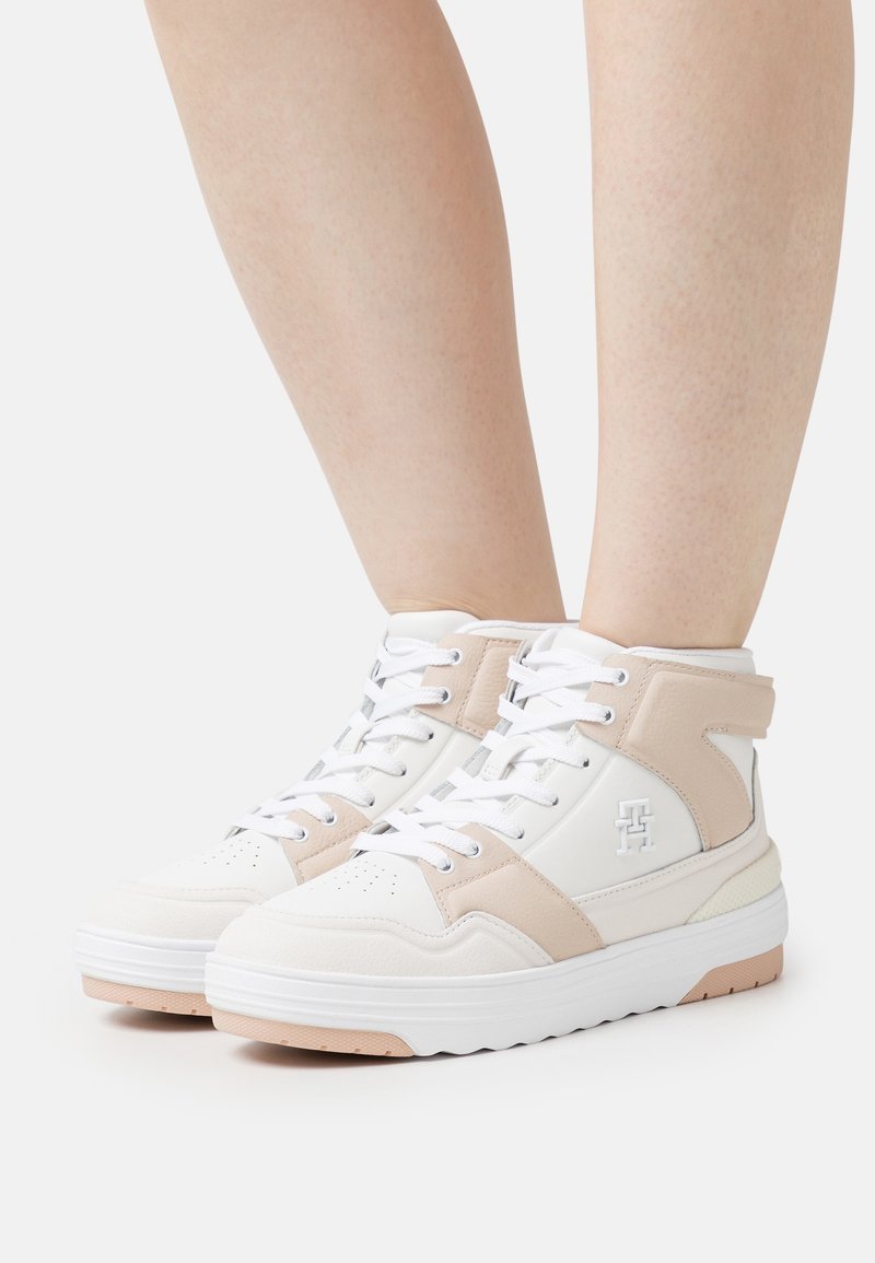 Baskets montantes blanches avec des accents beiges. Conçues en cuir et matériaux synthétiques, avec un col rembourré et une semelle épaisse.