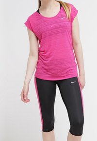 Rosa träningslinne med korta ärmar och ett strukturerat mönster, i kombination med svarta capribyxor med rosa sidodetaljer och en logotyp.