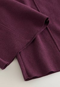 Vêtement tricoté en violet profond avec une finition texturée, présentant un ourlet replié et un design côtelé pour plus de détails.
