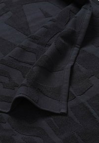 Tessuto nero con un motivo testurizzato, piegato con lettere in rilievo visibili. Il tessuto appare morbido e intrecciato con una finitura uniforme.