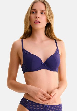 Soutien-gorge rembourré violet avec texture côtelée, dentelle sur les bords et détail de nœud au centre. Comprend des bretelles réglables et une finition lisse.