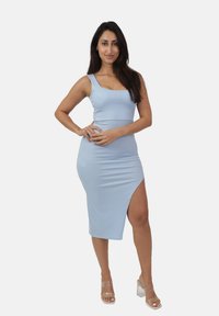 Abito midi a coste di un blu chiaro con scollatura quadrata, spacco laterale e silhouette aderente. Abbinato a sandali con tacco a tronchetto trasparente.