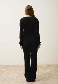 Ensemble en pull noir côtelé et pantalon large, avec une silhouette ajustée, des manches longues et une texture douce. Design minimaliste sans embellissements.