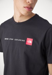 Zwarte katoenen T-shirt met een ronde hals, korte mouwen en een borstprint met witte tekst en een rood vierkant logo van The North Face.