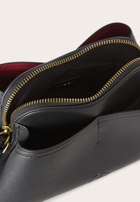 Sort lædertaske med gyldne lynlåse, der har en glat tekstur og rød indvendig foring. To rum er synlige, med et elegant design.