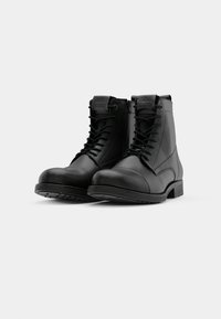 Botas negras de cuero hasta el tobillo con cordones y una cremallera lateral. Punta redondeada y suela de goma texturizada. Acentos cosidos en el cuerpo.