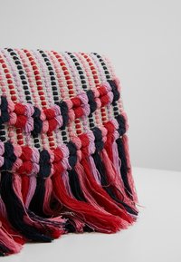 Borsa in tessuto intrecciato con motivo rosso, rosa e blu navy, caratterizzata da bordi frangiati. Superficie texture con disegni a punti alternati e intrecciati.