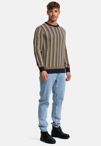 Pull en tricot rayé marron, crème et marine, avec des poignets et un ourlet côtelés. Associé à un jean bleu clair et des bottes noires à lacets.